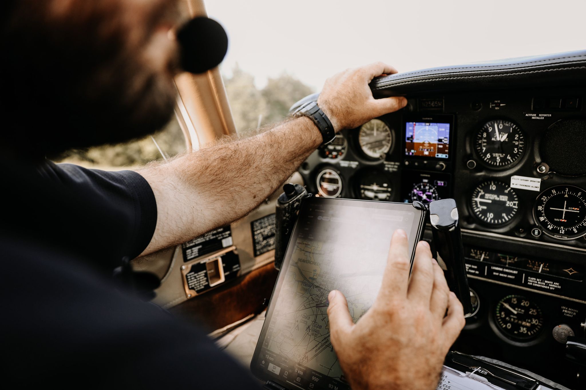 A pilot uses a tablet for navigation in a cockpit filled with aviation controls.